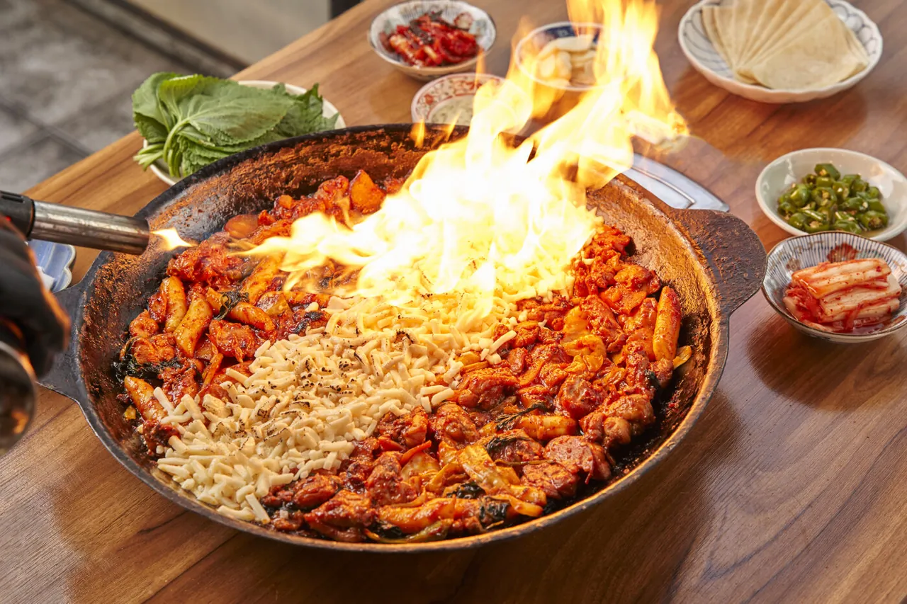회식 테이블에서 토치로 치즈를 녹이며 불꽃이 올라오는 닭갈비 철판